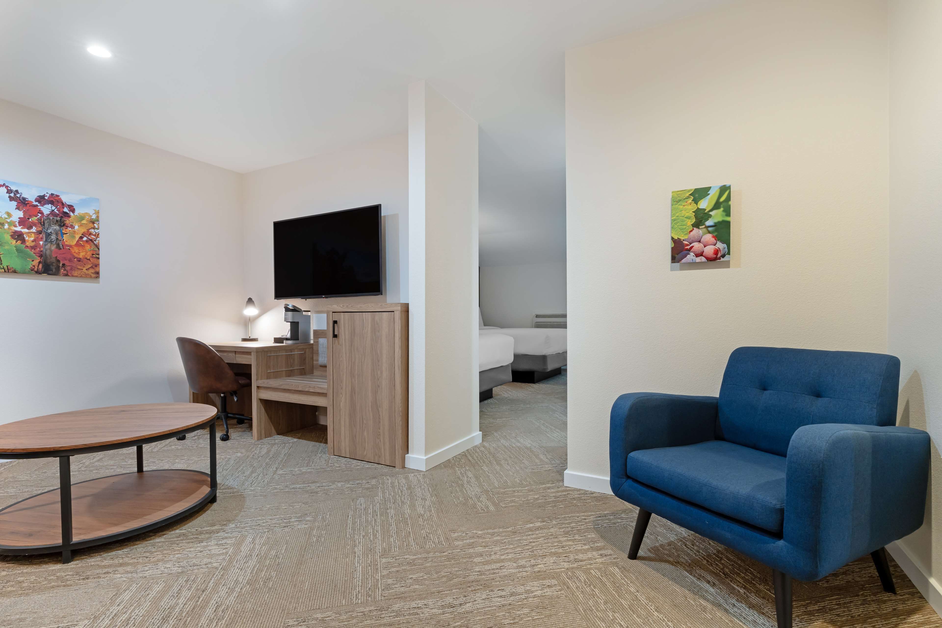 Habitación de hotel con escritorio, silla, televisión y un sillón azul.
