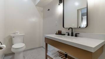A modern bathroom with a white toilet, a white sink with a black faucet, a mirror, and a towel rack.