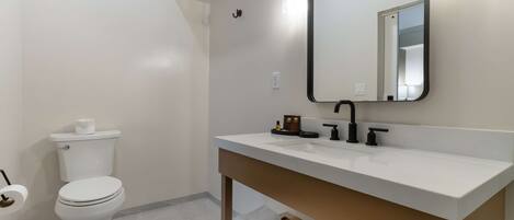 Un baño moderno con inodoro blanco, un lavamanos blanco con grifo negro, un espejo y un perchero para toallas.