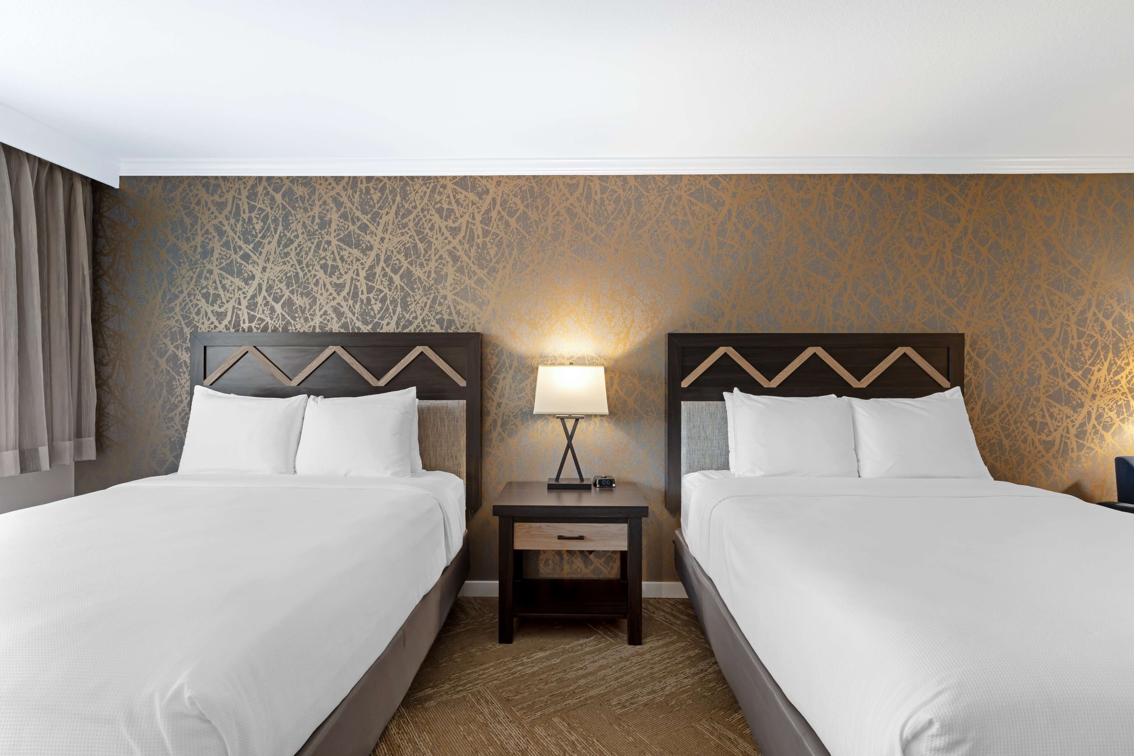 Ein Hotelzimmer mit zwei Betten, einem Nachttisch mit Lampe und einer Wand mit Muster.