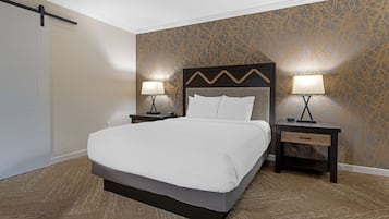 Une chambre d’hôtel avec un grand lit, deux tables de chevet avec des lampes, une tête de lit en bois et un papier peint à motifs.