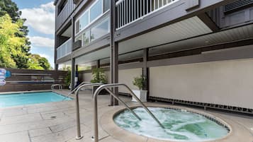 Un espace piscine comprenant un jacuzzi, une échelle en métal et un bâtiment doté de balcons.