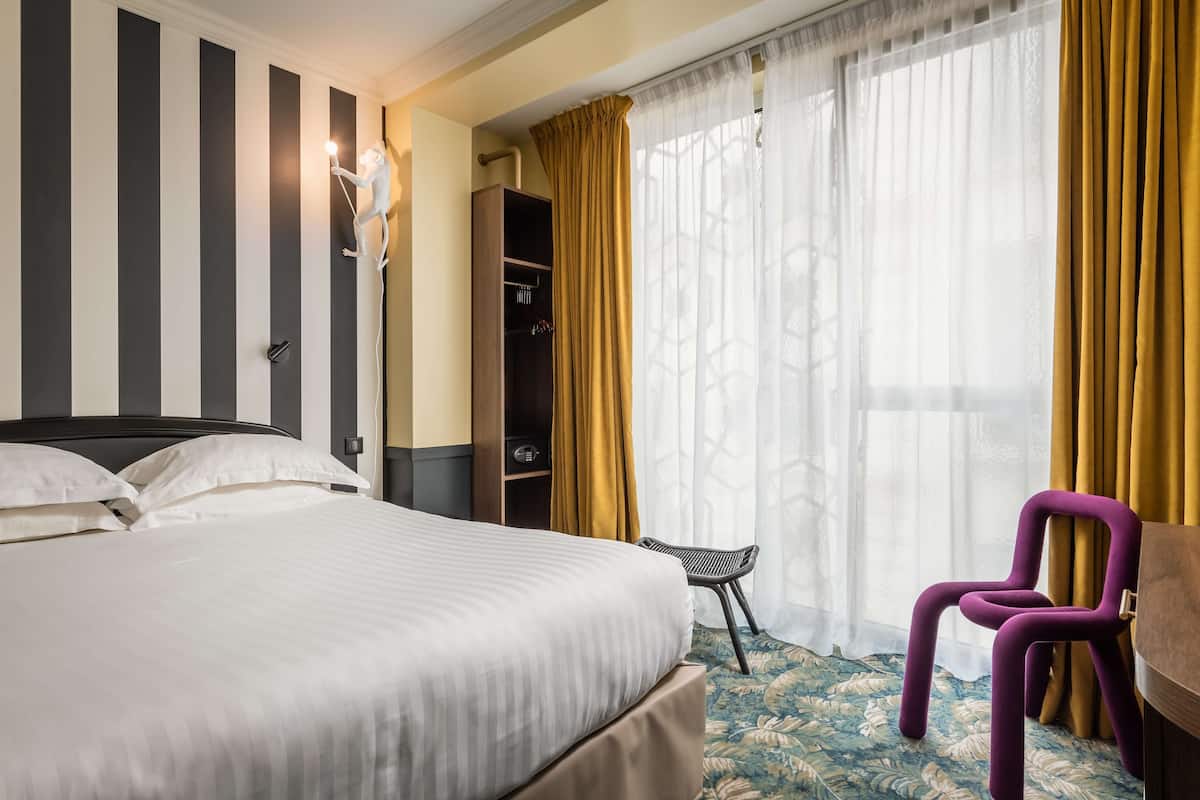 Quarto de hotel com cama, guarda-roupa, cadeira e secretária.