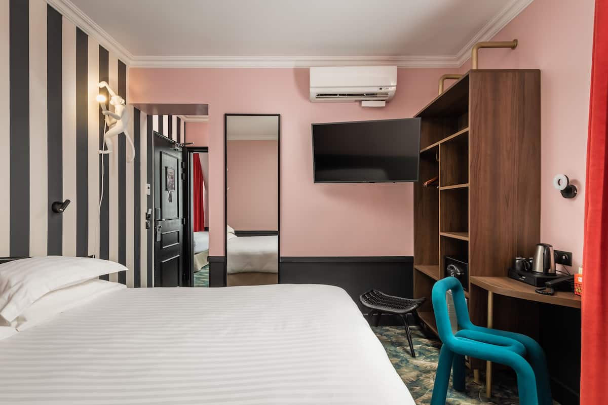 Quarto de hotel com cama, escrivaninha, cadeira, guarda-roupa, televisão e ar condicionado.