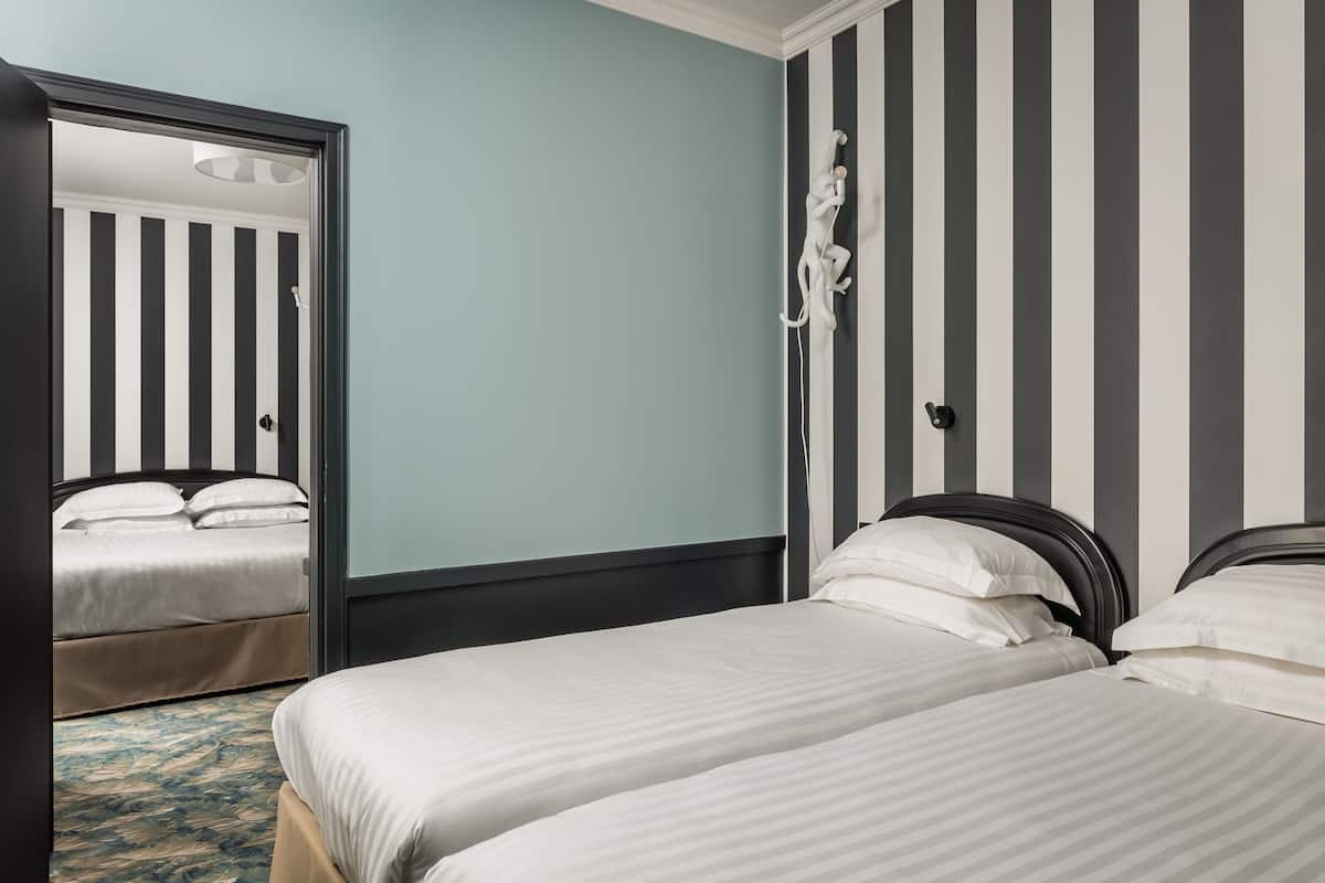Quarto de hotel com duas camas, uma parede listrada e um espelho.