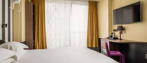 Una habitación de hotel con una cama grande, un escritorio con silla, un televisor y un armario.