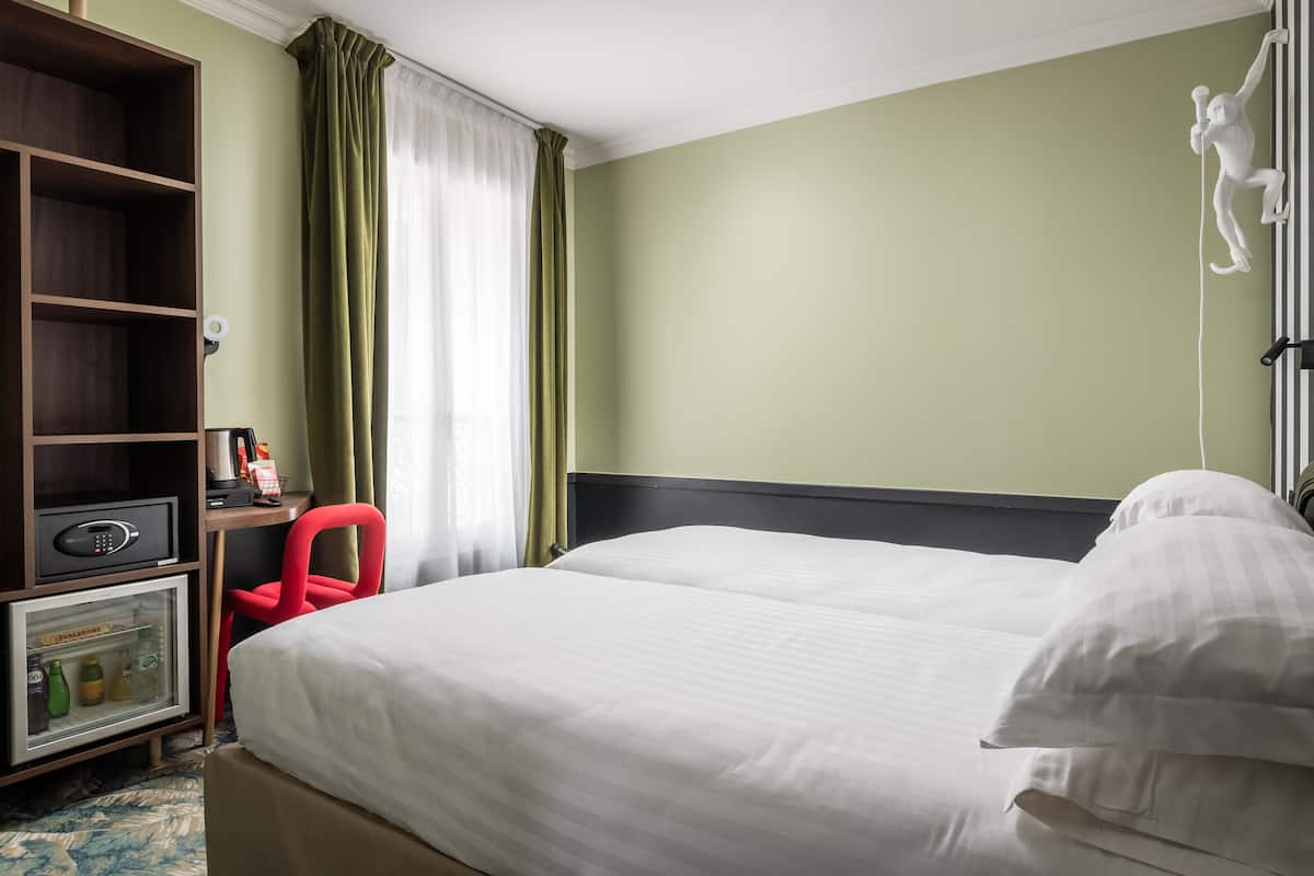 Quarto de hotel com uma cama, uma escrivaninha com computador, uma cadeira vermelha e um mini-bar.