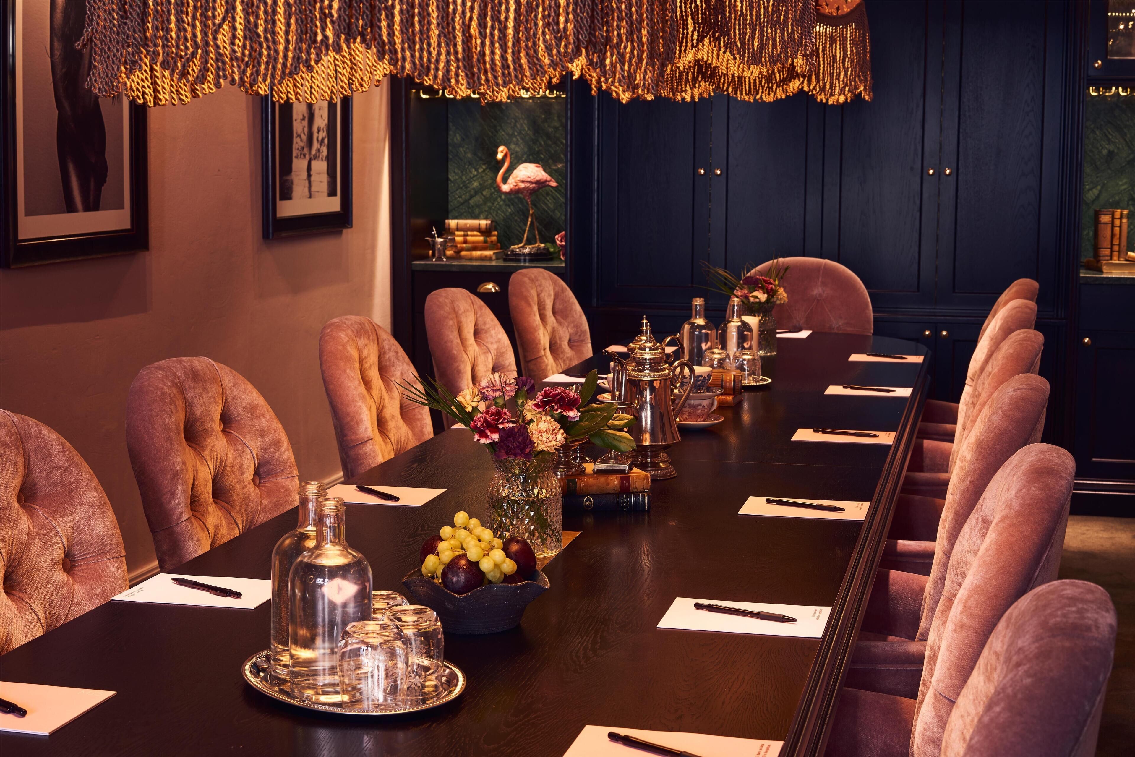 A conference room with a long table, plush chairs, and a decorative chandelier.