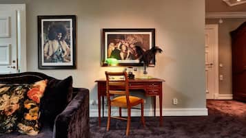 Una habitación con escritorio, silla y sofá con cojines florales. Hay dos cuadros en la pared.
