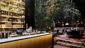 A bar area with a wooden counter, shelves with bottles, and a seating area with tables and chairs. - MJ's (Malmö)