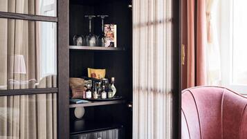 A room with a dark wooden bookshelf, a pink chair, and a window with curtains.