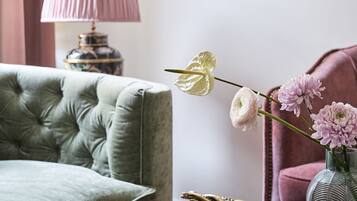 A green sofa, a pink lamp, a framed picture, a vase with flowers, and a stack of books.