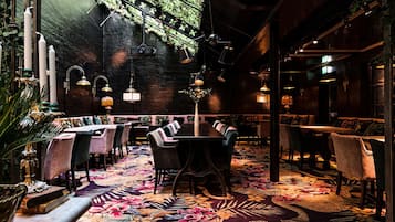 A dimly lit restaurant with a cozy ambiance, featuring plush seating, a patterned carpet, and hanging lights.