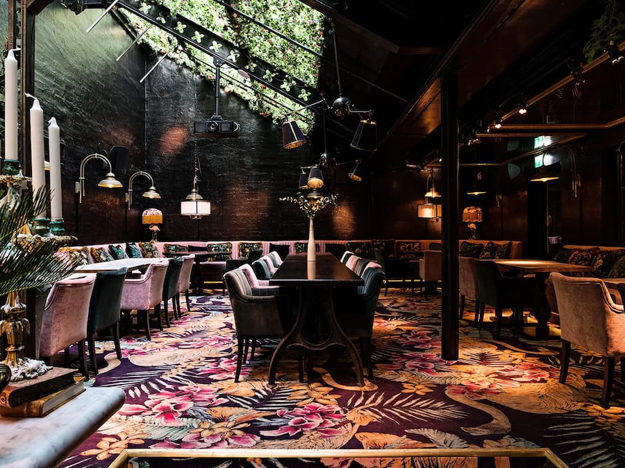 A dimly lit restaurant with a cozy ambiance, featuring plush seating, a patterned carpet, and hanging lights.