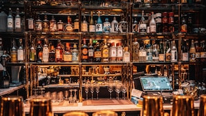 A bar with shelves of various liquor bottles and glasses. - MJ's (Malmö)