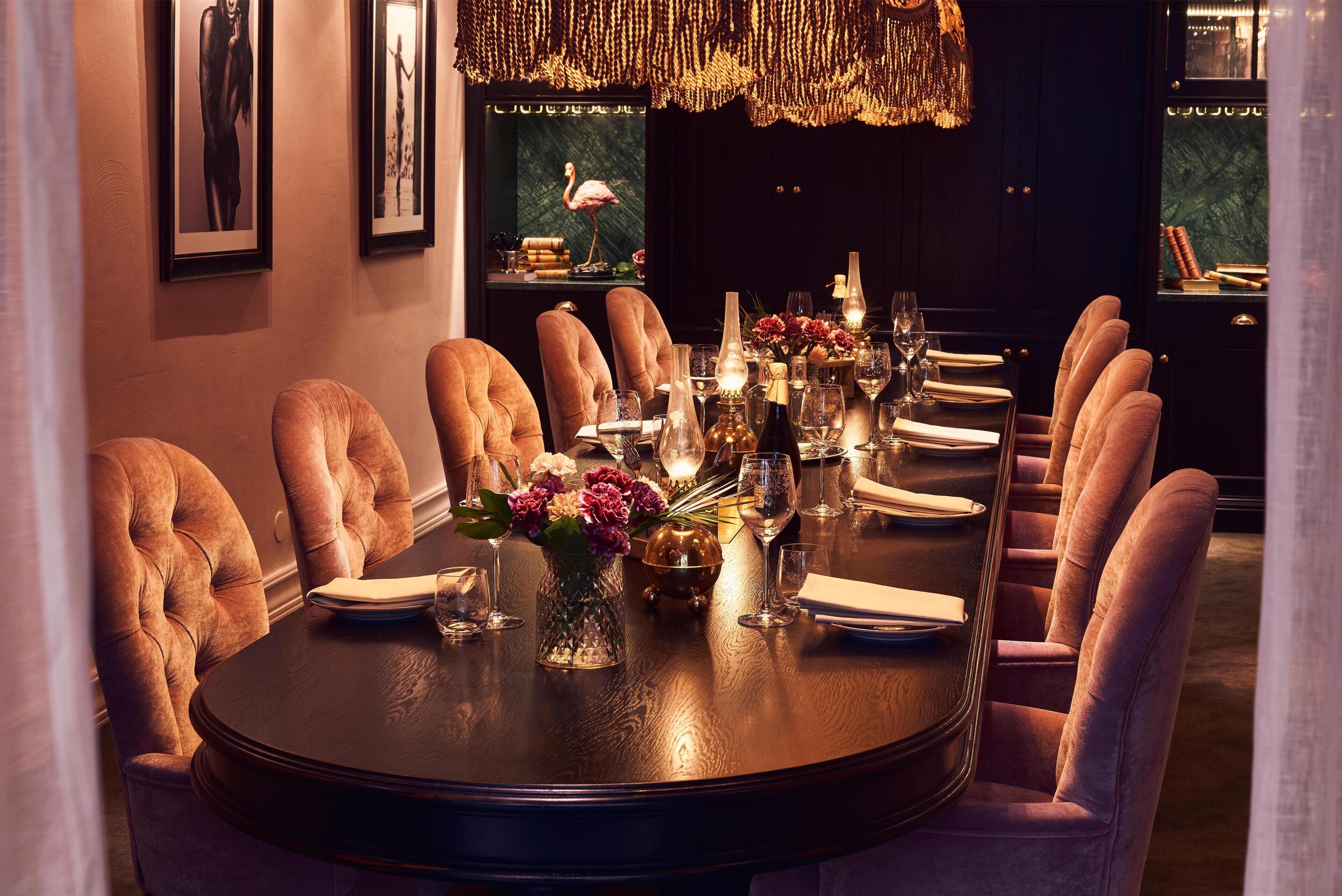 Une salle à manger élégante, avec une table ronde dressée pour huit personnes, entourée de fauteuils confortables et agrémentée de compositions florales et de bougies.