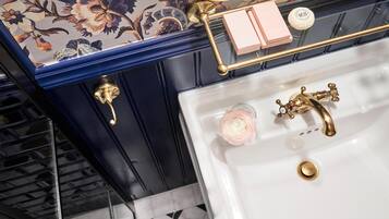 Un baño con lavamanos blanco, detalles dorados y un diseño de papel tapiz floral.