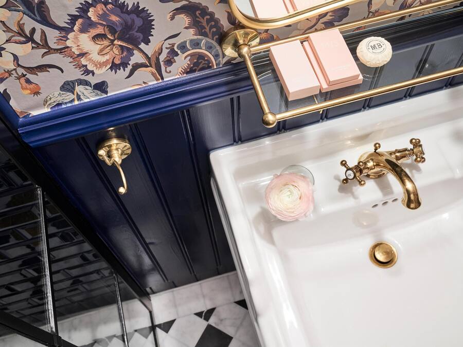 Un baño con lavamanos blanco, detalles dorados y un diseño de papel tapiz floral.