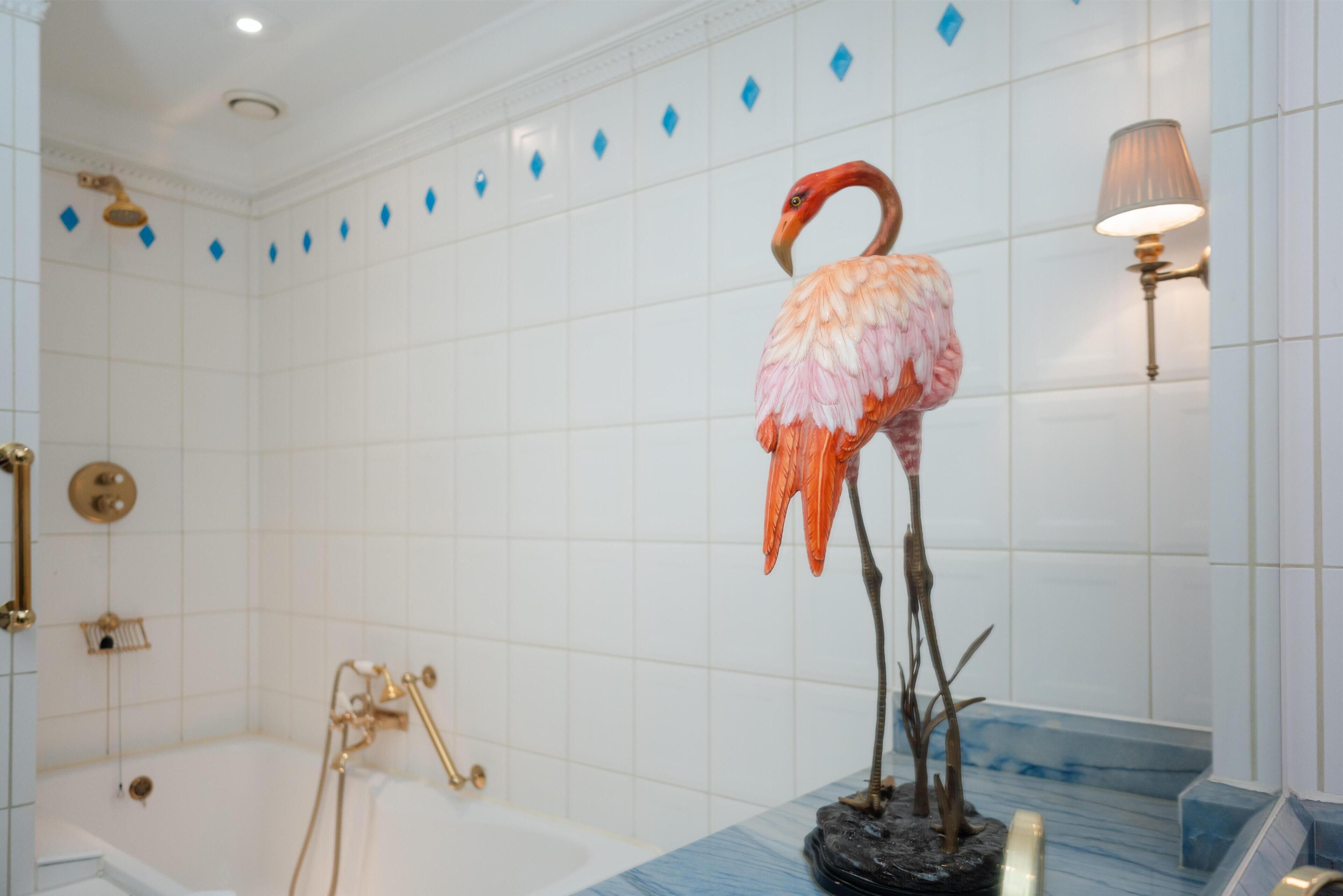 Ett badrum med badkar, dusch och en dekorativ flamingo-staty.