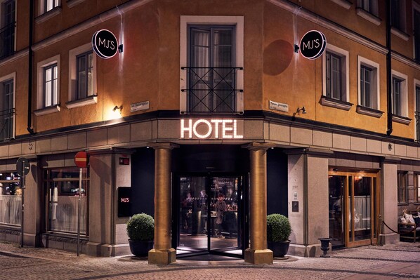 A hotel entrance with a glass door, a sign above the door, and two potted plants on either side.