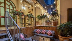 Un espace extérieur aménagé avec un canapé, des chaises et une table, entouré de plantes en pot et d’une clôture en bois.