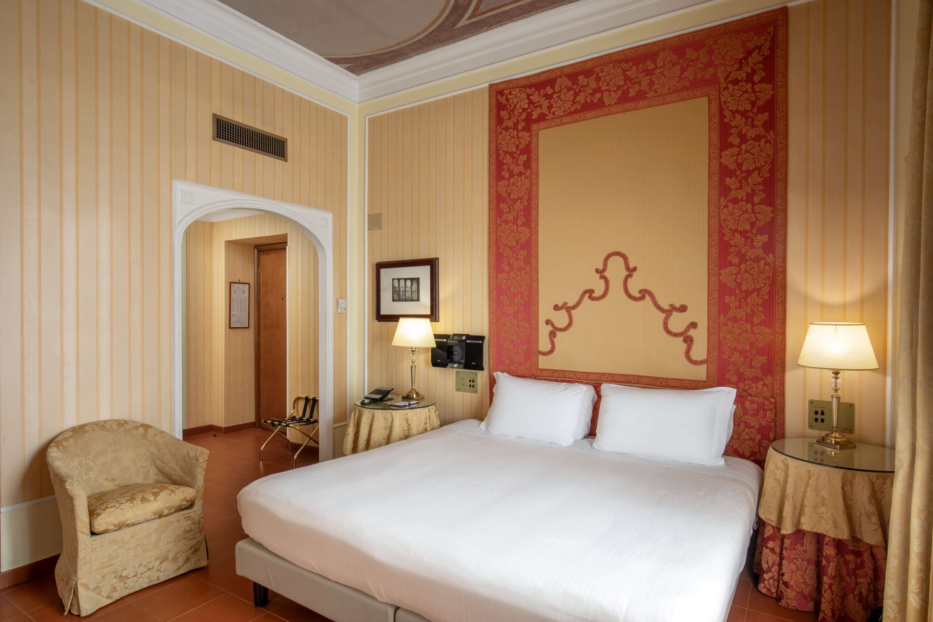 Une chambre d’hôtel avec un grand lit, une chaise, un bureau avec une lampe et un panneau décoratif au mur.