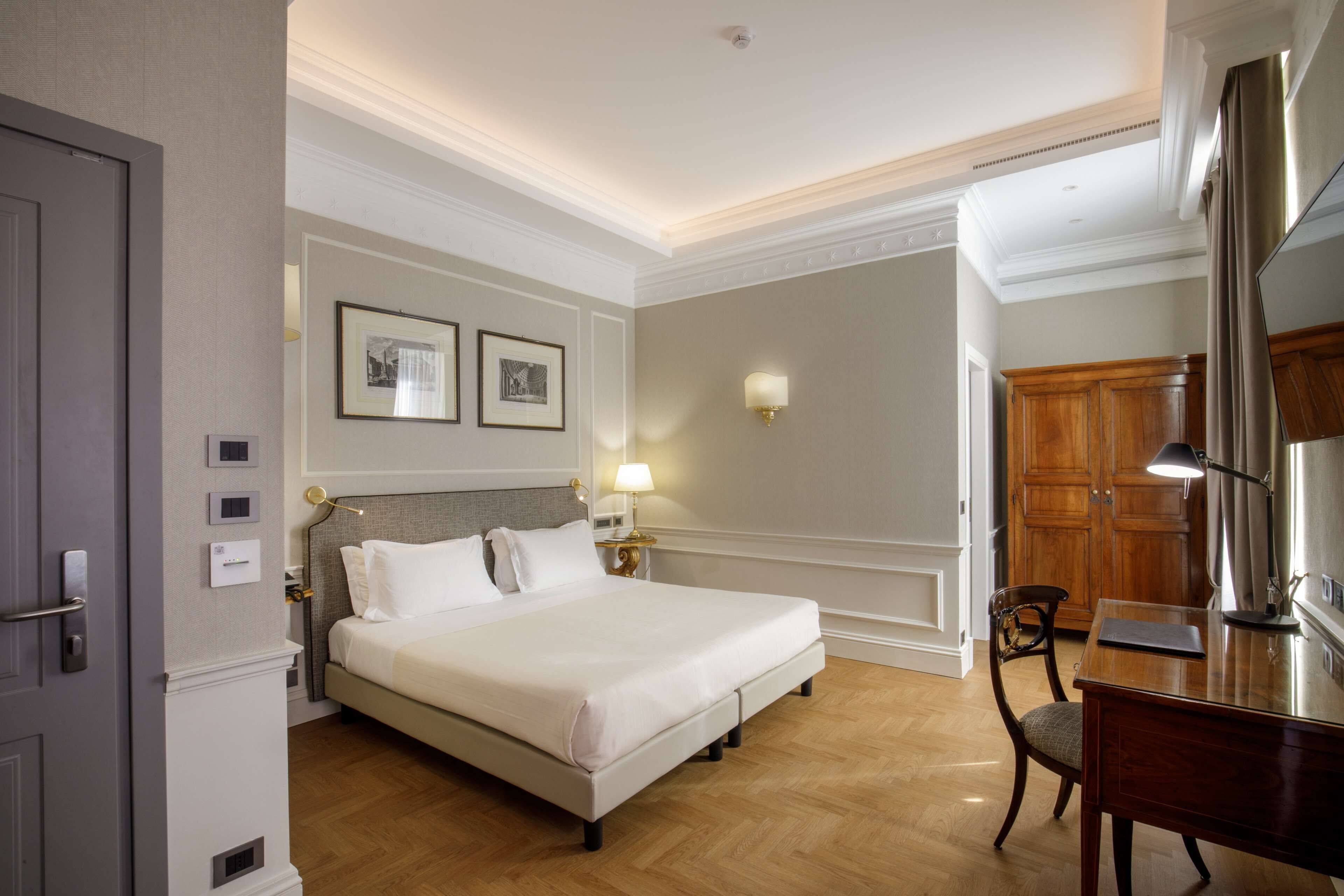 A hotel room with a large bed, a desk, a chair, and a wardrobe.