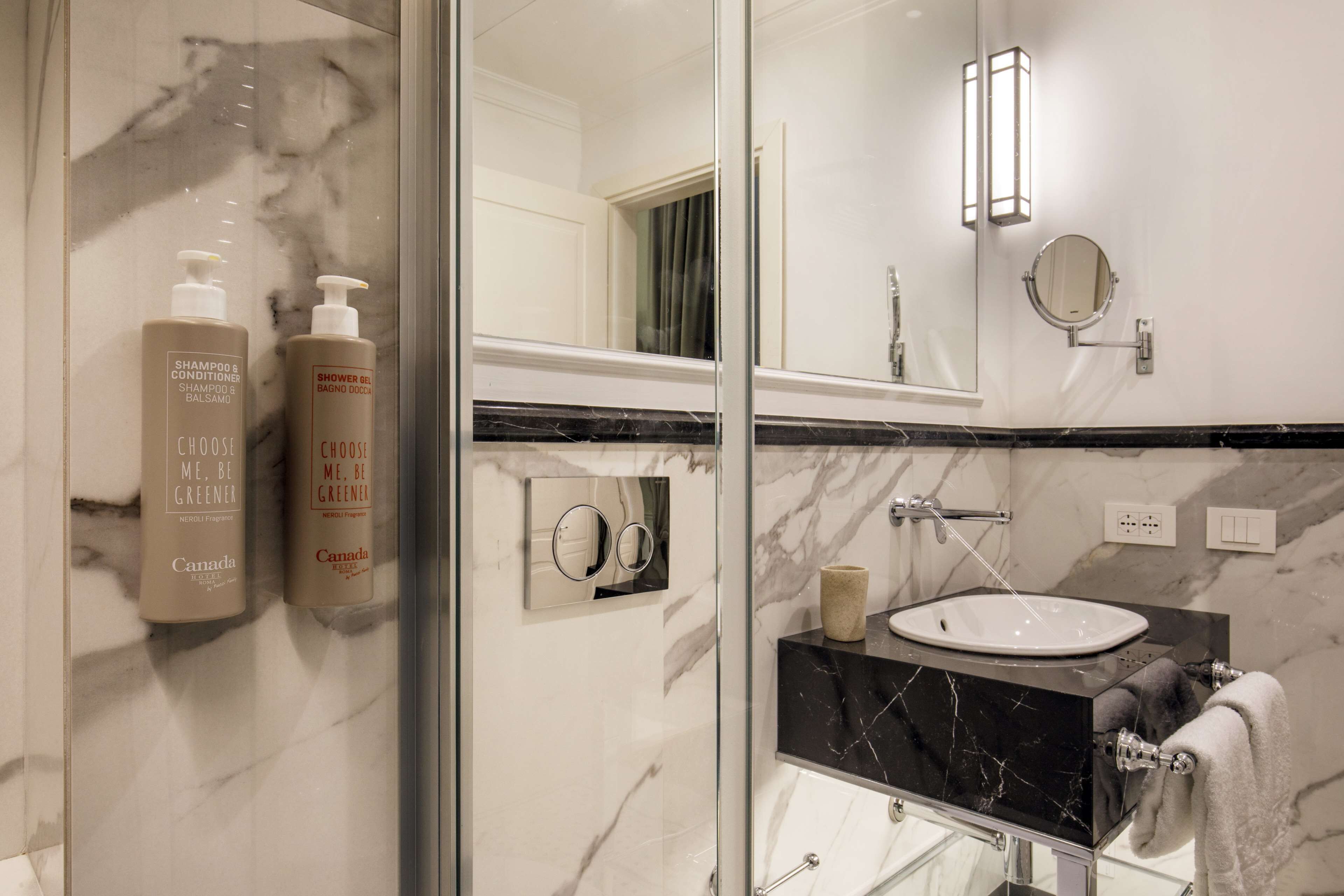 Une salle de bain moderne avec une douche à l’italienne en verre, un lavabo en marbre et des articles de toilette fixés au mur.