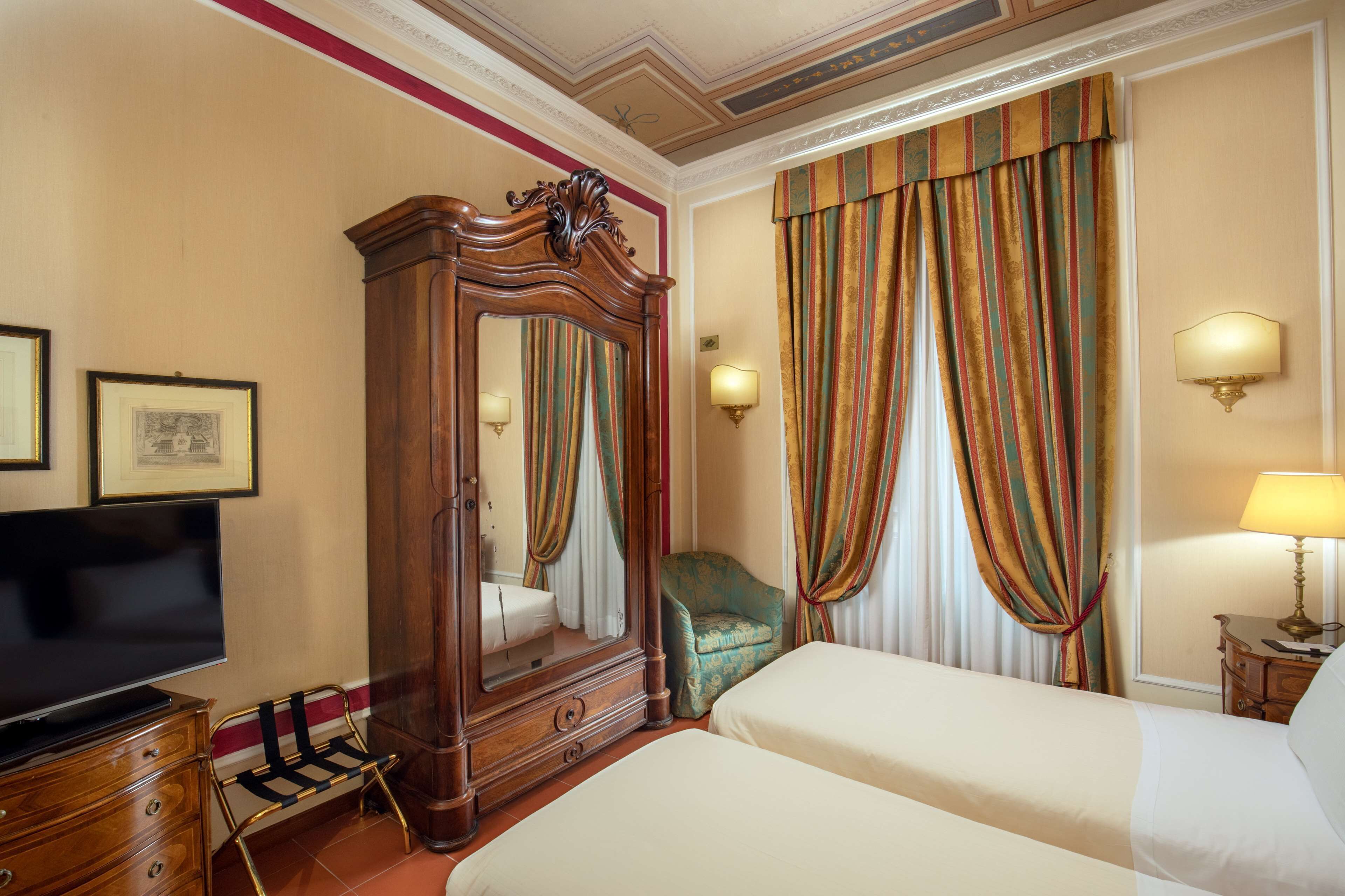 Una habitación de hotel con un espejo grande, televisión, dos camas, una silla y cortinas.