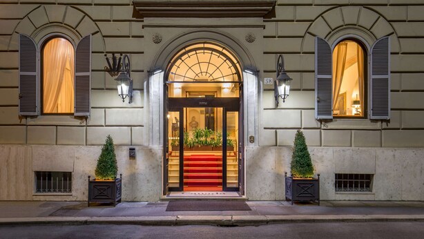 L’entrée d’un hôtel, avec un tapis rouge, deux sapins de Noël en pot et une statue au-dessus de la porte.