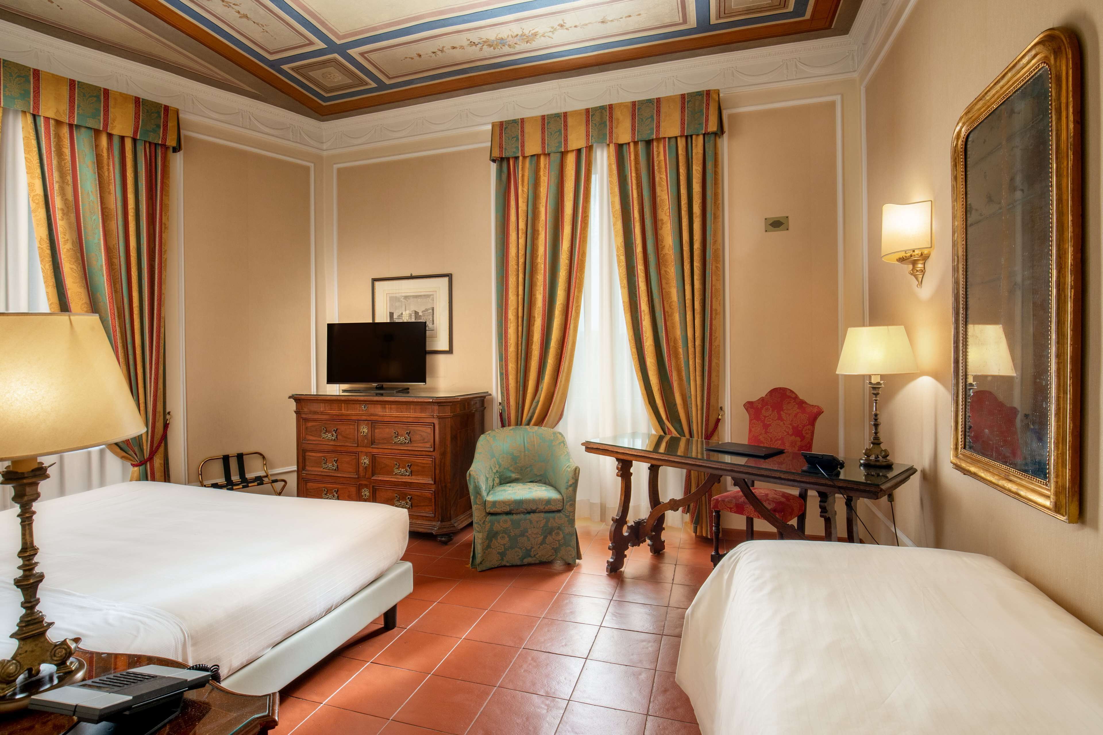 A hotel room with two beds, a television, a dresser, a chair, and a desk with a lamp.