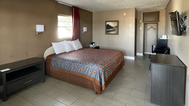 Habitación de hotel con una cama grande, un escritorio, una silla, un televisor y un baño pequeño.