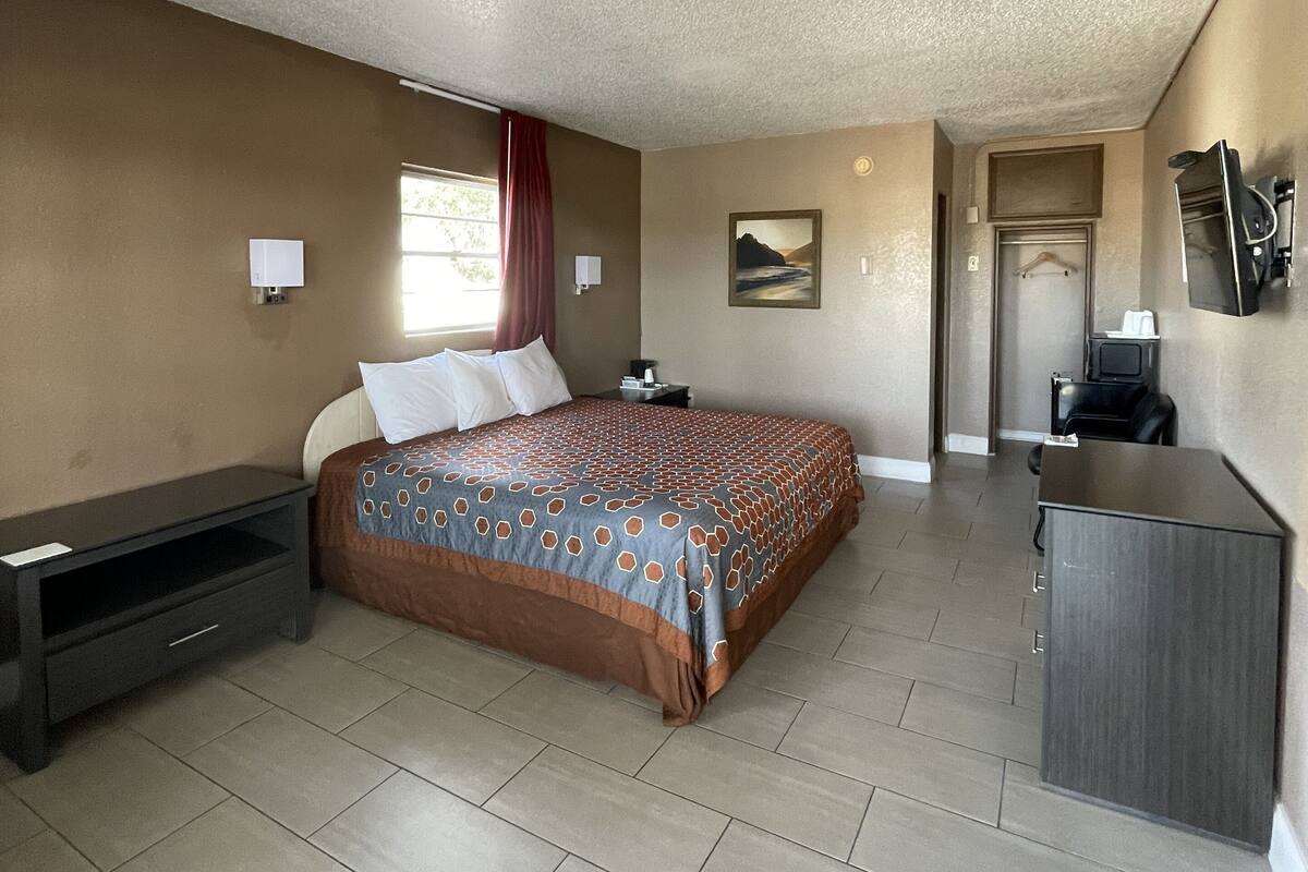 A hotel room with a large bed, a desk, a chair, a TV, and a small bathroom.