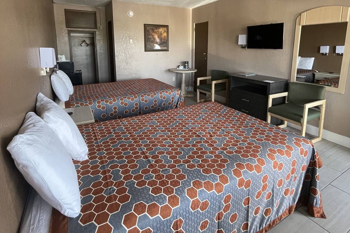 A hotel room with two beds, a desk, a chair, a television, and a mirror.