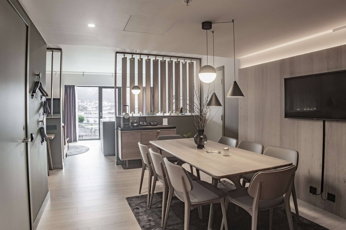 A modern dining area with a wooden table and chairs, a vase with branches, and pendant lighting.