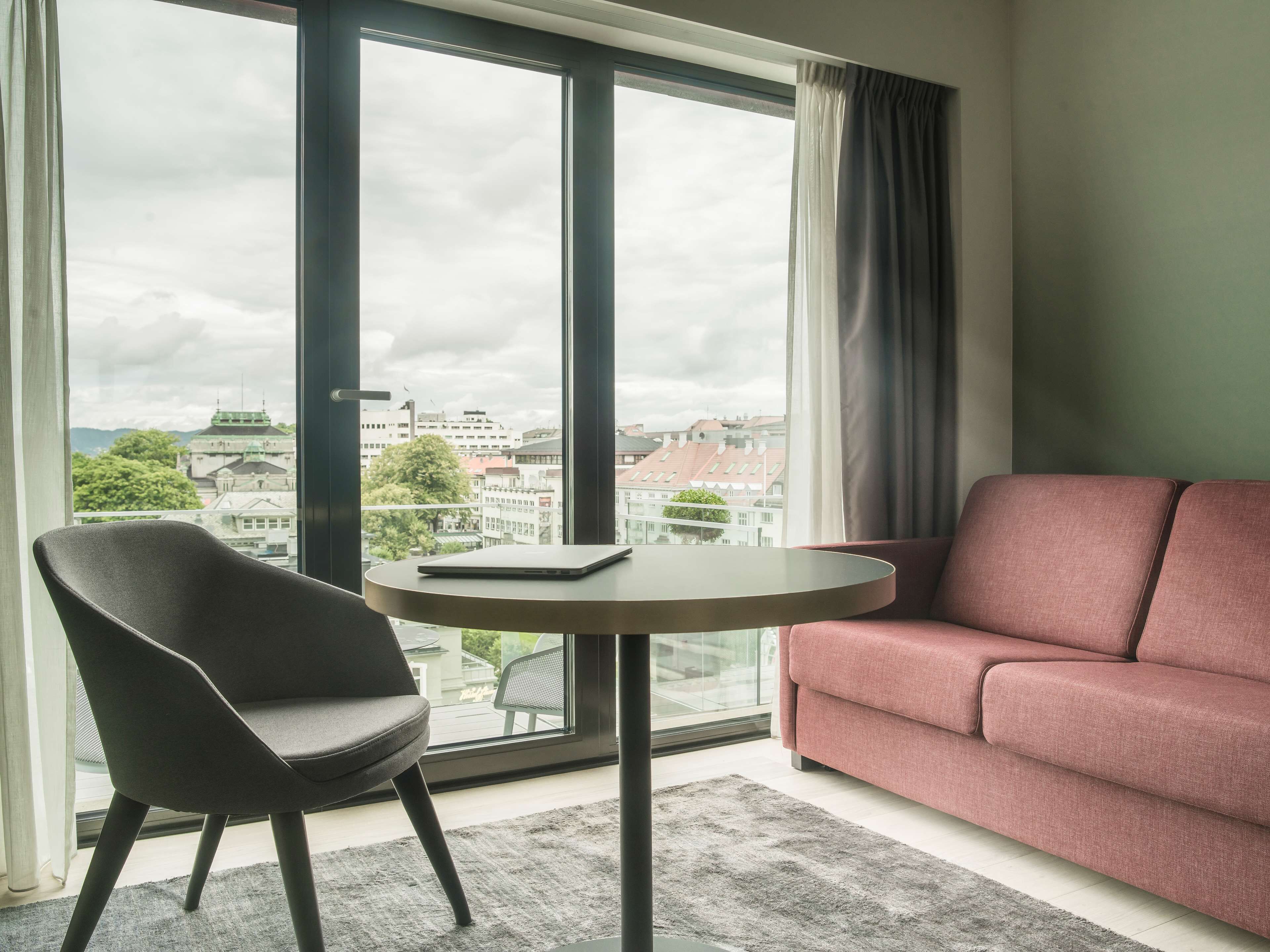 Une pièce moderne avec une grande fenêtre, une table ronde, une chaise noire et un canapé rouge.