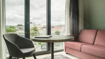 A modern room with a large window, a round table, a black chair, and a red sofa.