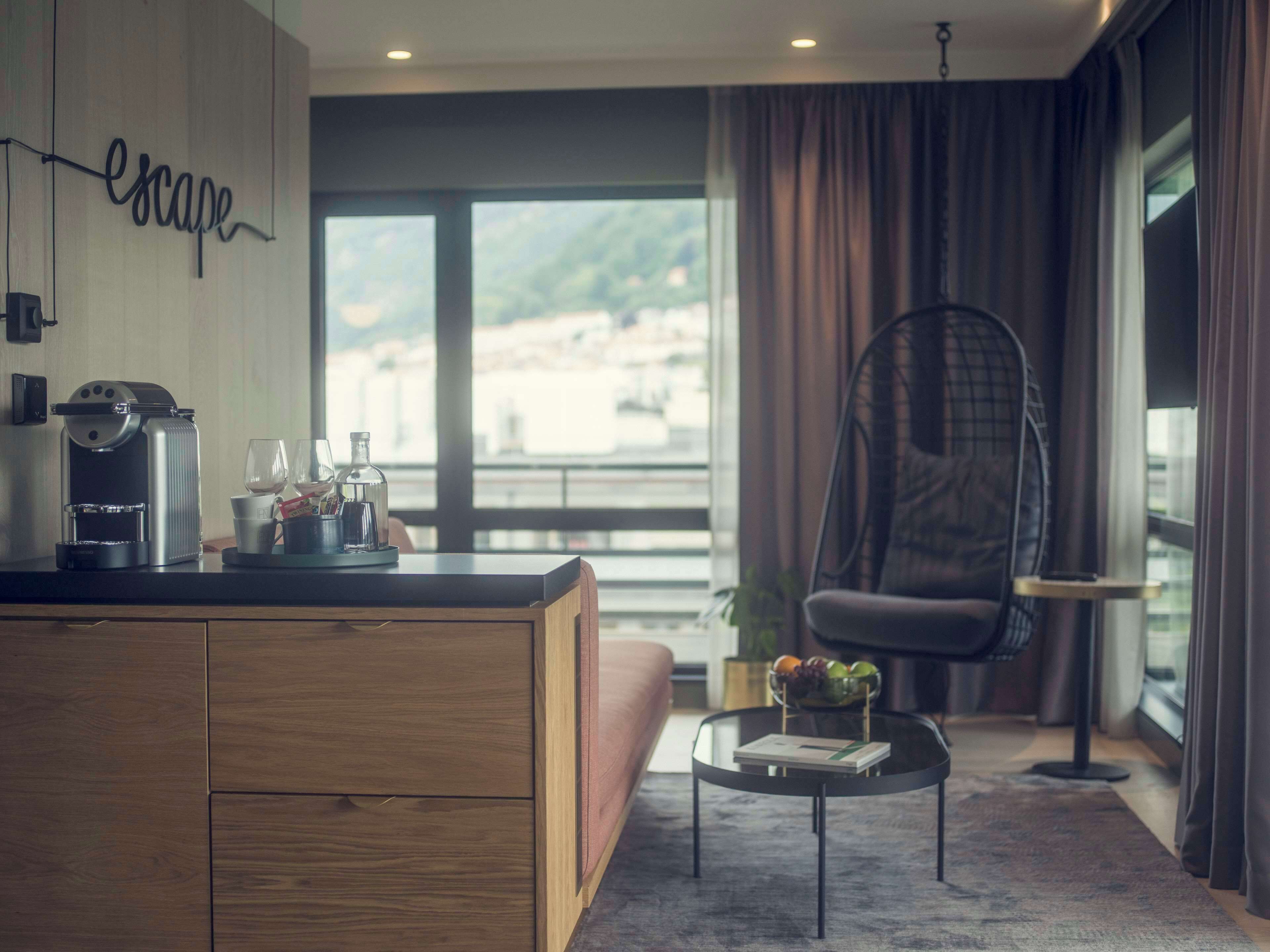A modern living room with a wooden cabinet, a coffee machine, and a glass table with a book and fruit bowl.