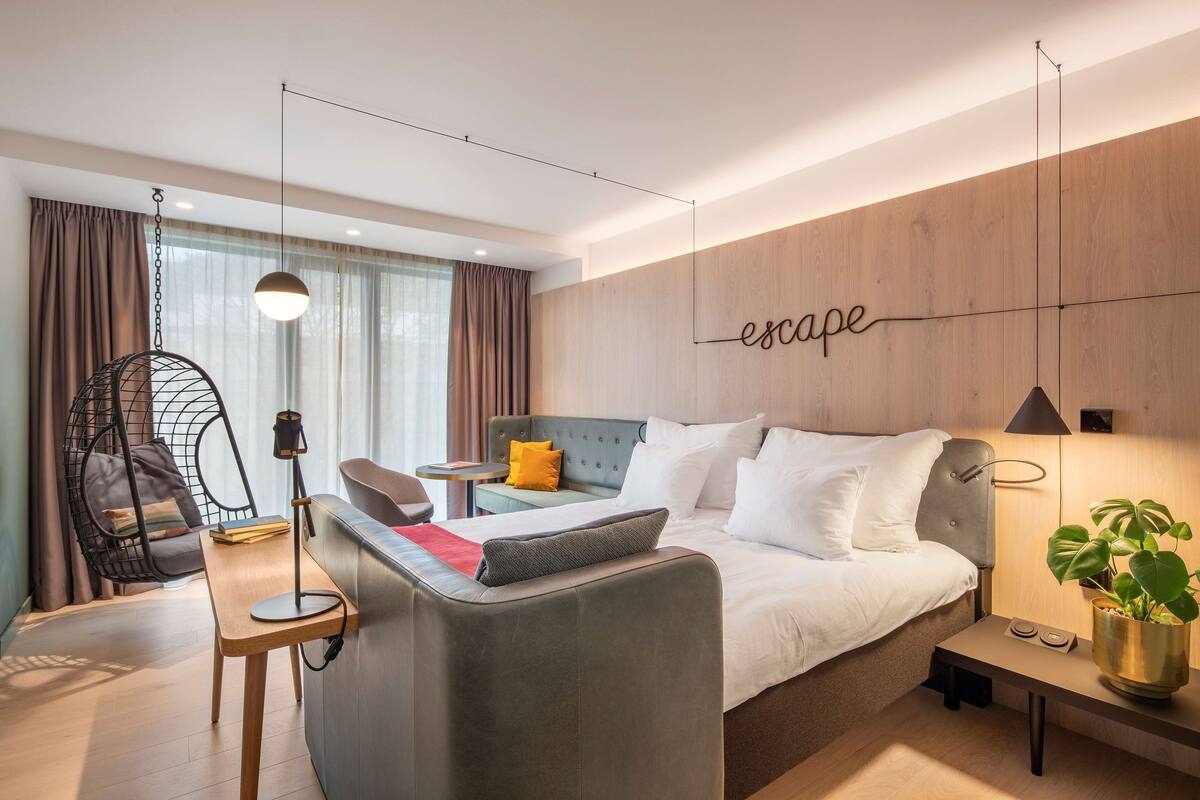 A modern hotel room with a bed, a sofa, a desk, and a hanging chair.