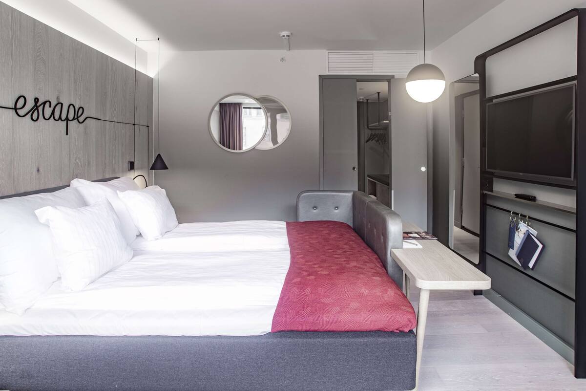 A modern hotel room with a large bed, a small desk, a TV, and a mirror.