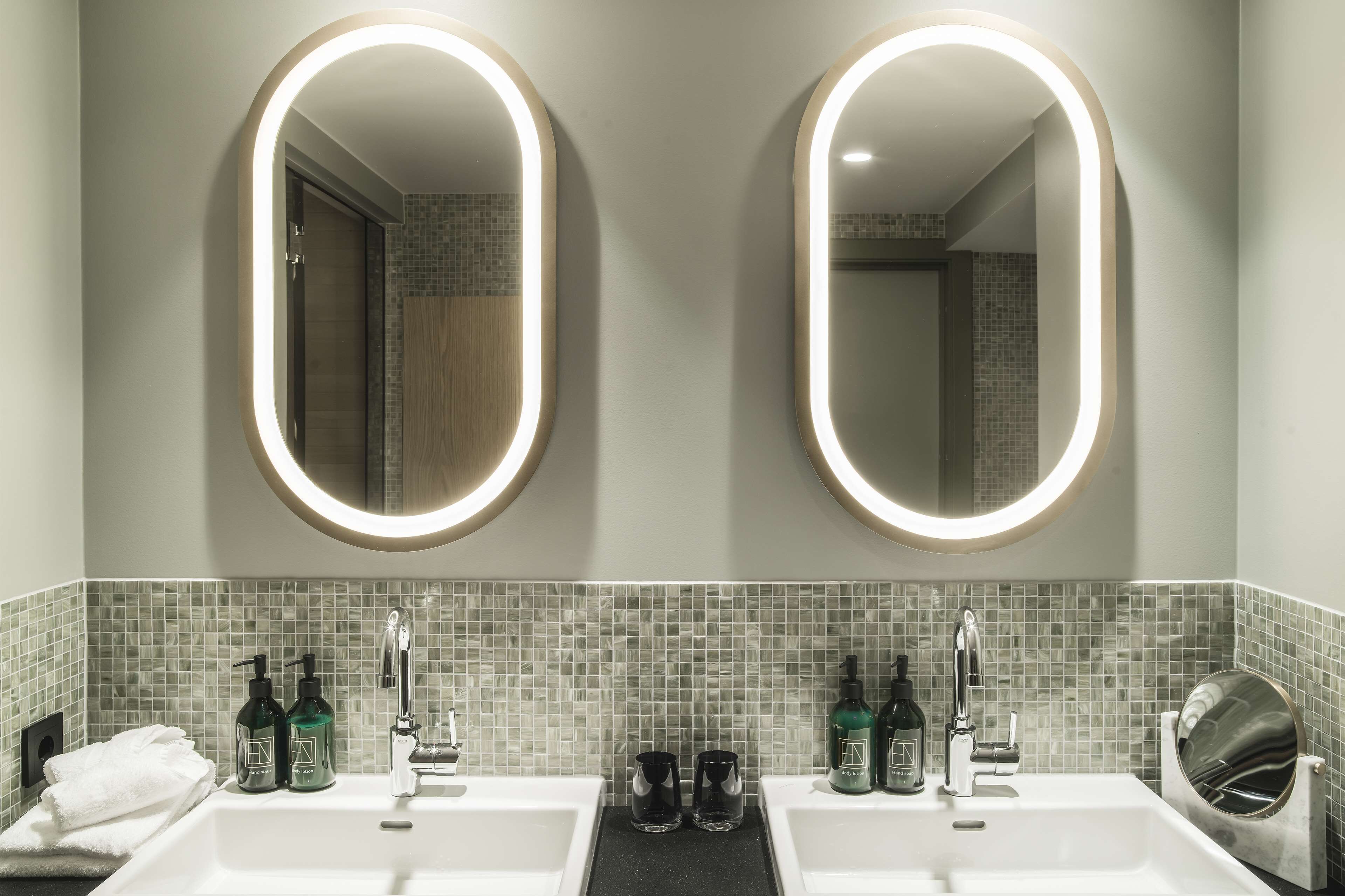 Un baño con dos lavamanos, cada uno con un espejo encima. Hay botellas de champú y acondicionador en el mostrador.