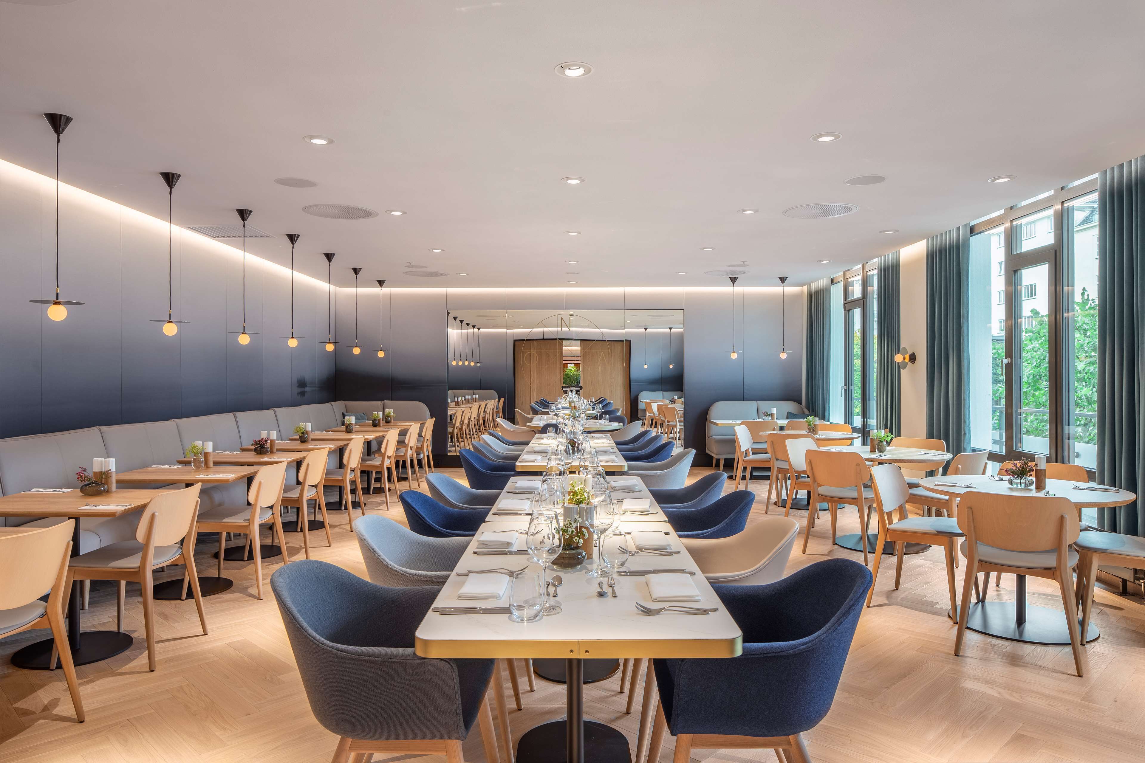 Un comedor moderno con mesas largas, sillas azules e iluminación colgante.