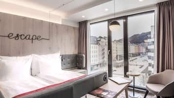 Una habitación de hotel moderna con un ventanal grande, una cama, una zona de estar y vistas a la ciudad.