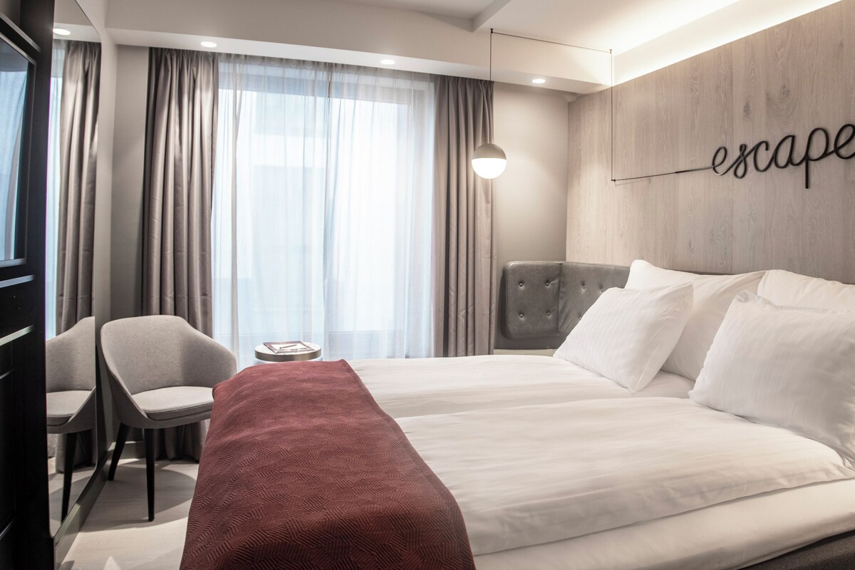 Habitación de hotel con una cama grande, un escritorio, una silla y un letrero en la pared que dice 'escape'.