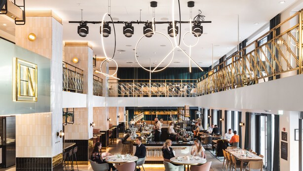 A modern restaurant with multiple dining areas, a bar, and a visible kitchen area.