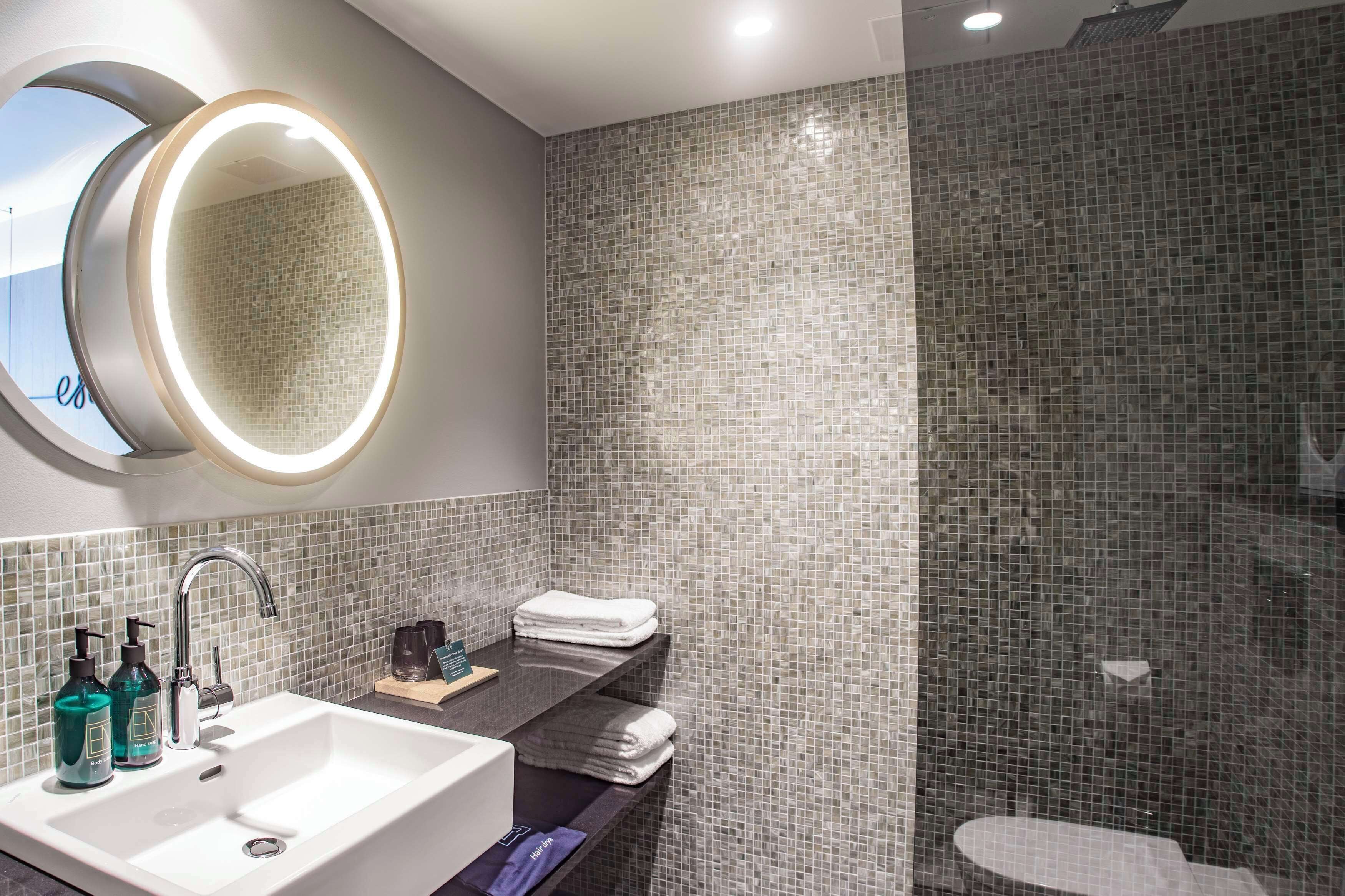 A modern bathroom with a large mirror, a sink with two bottles of soap, and a shower area with a tiled wall.