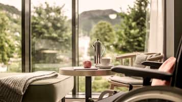 A wheelchair-accessible room with a view of greenery and hills, a small table with a cup and a pitcher, and a cozy seating area.
