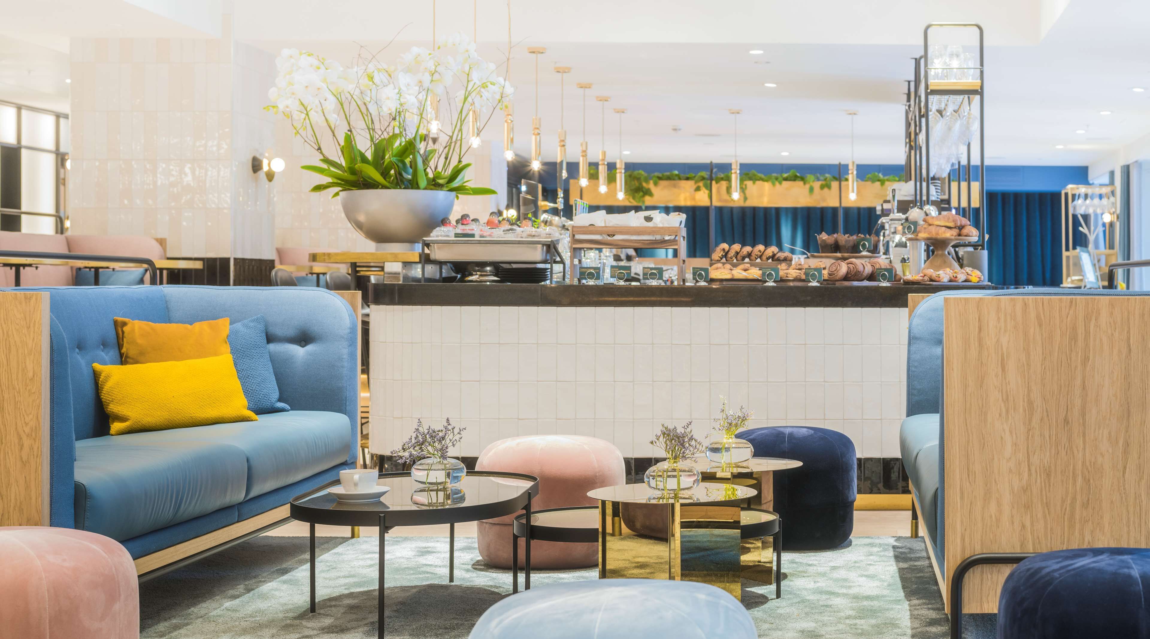 En moderne hotellobby med en blå sofa, et sofabord og et siddeområde med en pink skammel.