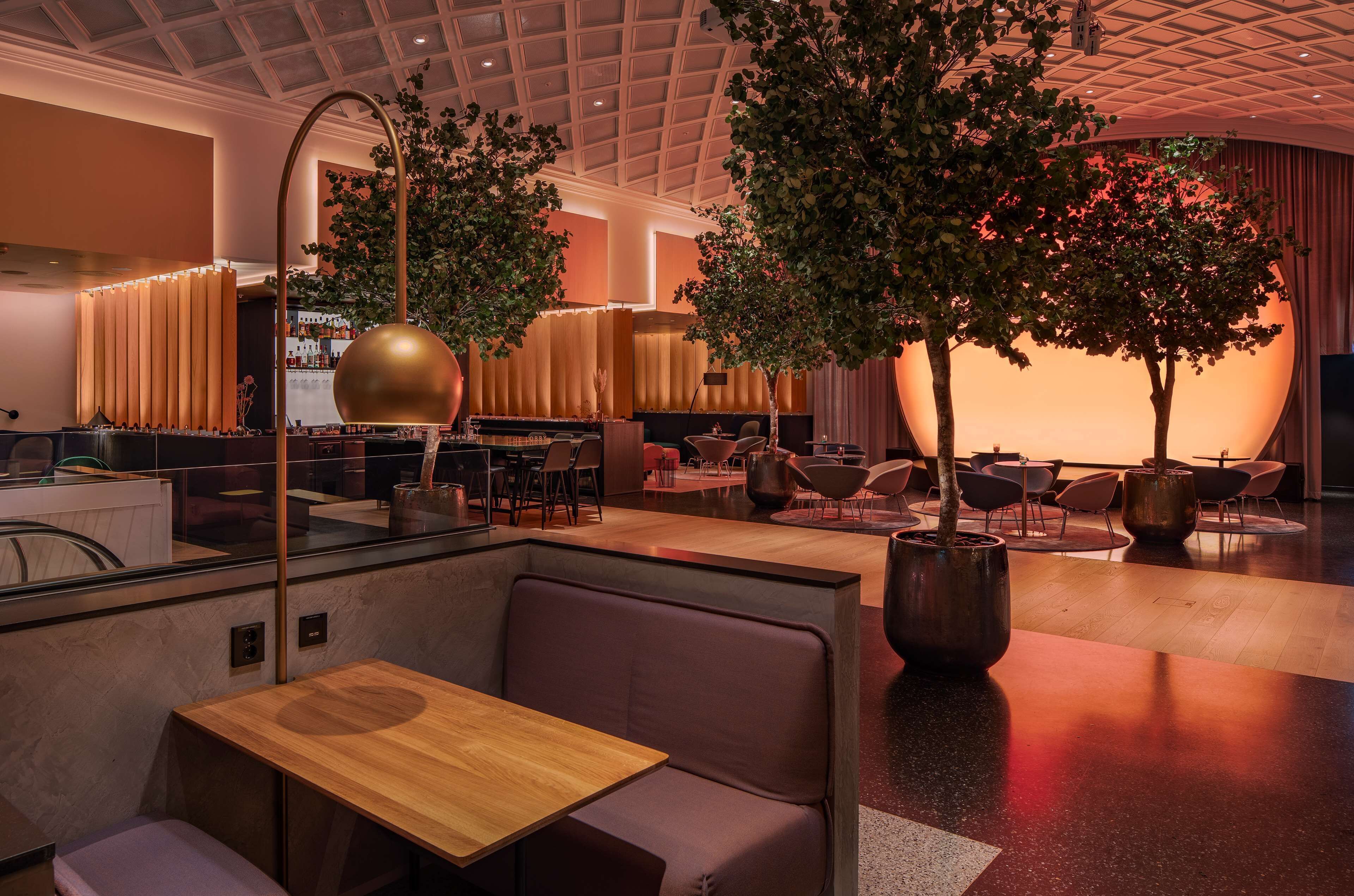 Un interior moderno con zonas de estar, un bar y un gran árbol en el centro.