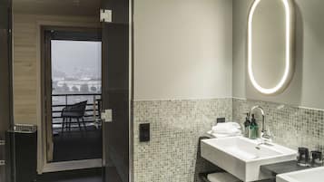 Un bagno moderno con un ampio specchio, un lavandino e una doccia. Si intravede un balcone con una sedia attraverso la porta.
